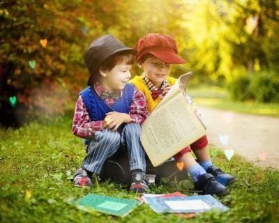 Otroka s pokrivali na glavi sedita v travi in bereta