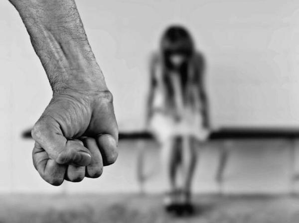 Roka stisnjena v pest, v drugem planu deklica na klopi s sklonjeno glavo