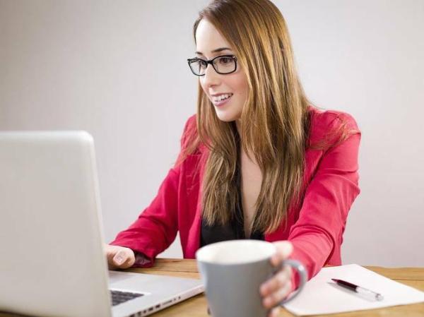 Uradnica za računalnikom in s kavo v roki