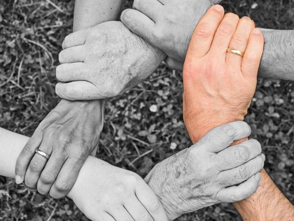 Roke, ki se držijo za zapestja. Ena je barvna, druge so črno bele.