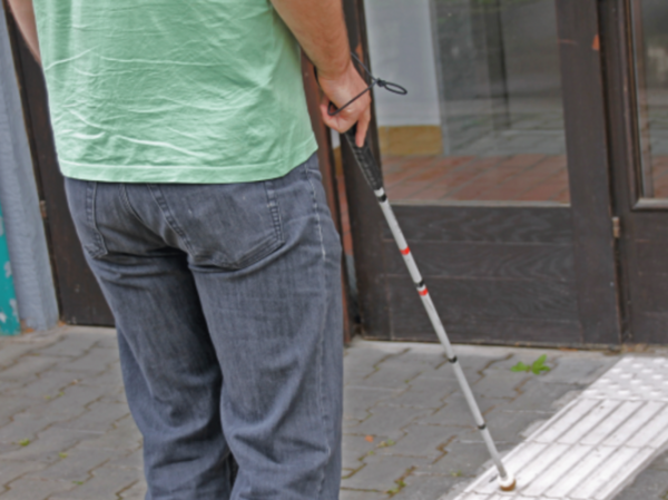 Oseba z belo palico pred vhodom v stavbo