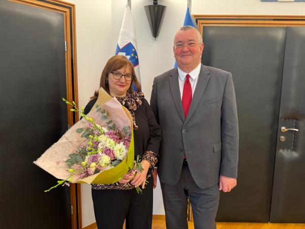 Primopredaja poslov med varuhinjo in namestnikom. Varuhinja v roki drži &scaron;opek rož.