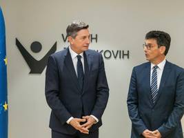 Predsednik republike Borut Pahor in varuh človekovih pravic Peter Ssvetina stojita pred steno, na kateri je znak institucije Varuha, levo se čuti zastava EU