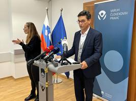 Varuh za govorniškim pultom predstavlja podrobnosti posebnega poročila o dostopnosti centrov za socialno delo, ob njem tolmačka za znakovni jezik tolmači, v ozadju pano z logotipom institucije Varuha