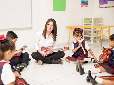 Otroci in učiteljica sedijo na tleh z inštrumenti