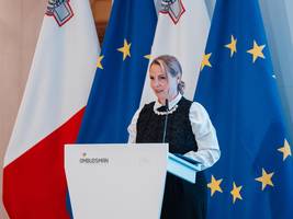 [Translate to English:] Namestnica varuha dr. Dijana Možina Zupanc za govorniškim pultom. V ozadju so zastave. 